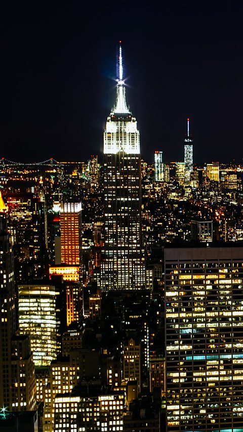 Photograph of the Empire State building lit up at night, surrounded by other buildings.