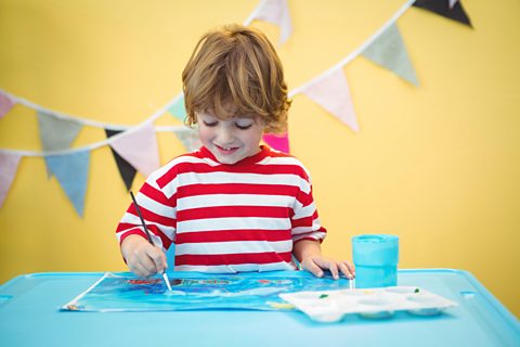 A young boy wearing a red-and-white striped t-shirt painting at a table