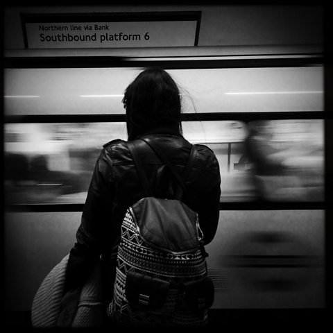 A black and white photo of girl on train platform