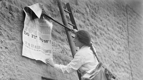 Photograph of a girl posting a World War One recruitment poster on the side of a building