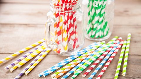 A collection of colourful paper straws displayed in two clear jars and on a wooden table.