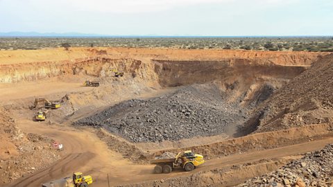 A large open pit for manganese mining with yellow trucks and diggers.