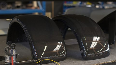 Carbon-reinforced plastic (CRP) mudguard parts for automobiles sit on a table.