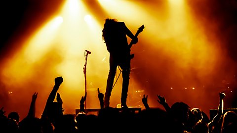 Silhouette of crowd at rock concert watching person on stage with a guitar.