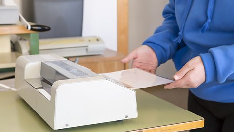 A woman’s hands feeding a document through a laminating machine.