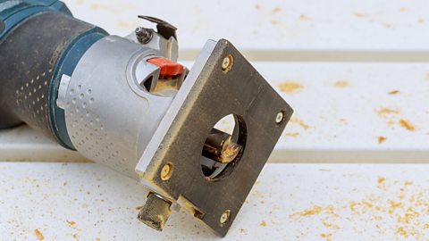 A hand-held silver router with a flat, square, metal base used for wood.