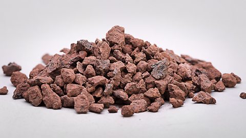A heap of small clusters of natural iron ore in a red shade, isolated on a white background.