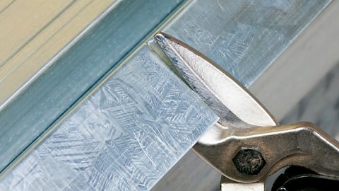 A close-up image of tin snips cutting a piece of steel.