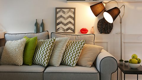 A modern living room with a grey sofa, many textile cushions and a large lit floor lamp.