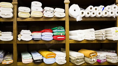 A shelving unit in a fabric shop featuring various rolls  of fabric on the shelves.