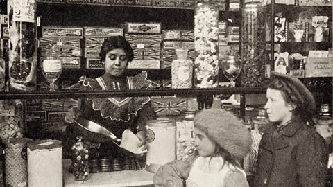 A shopkeeper serving sweets to two children in the early 1900s