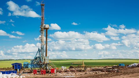 A landscape image of an oil rig site with a grassy hillside and blue sky.