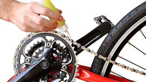 A man’s hand shown oiling a bike chain.