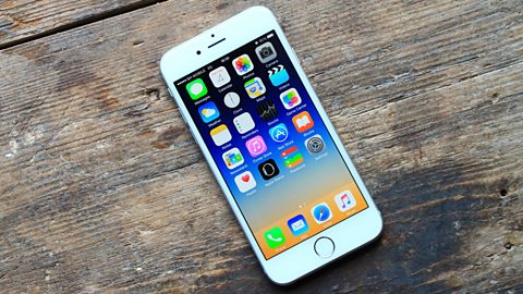 A turned on white iPhone 6 placed on a modern wooden table.