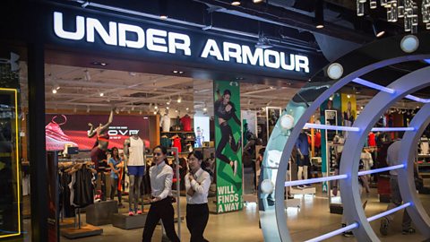 An Under Armour shopfront inside a shopping centre with two women walking past.