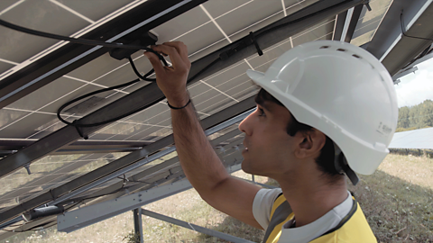 A young man checks cables at a solar power farm