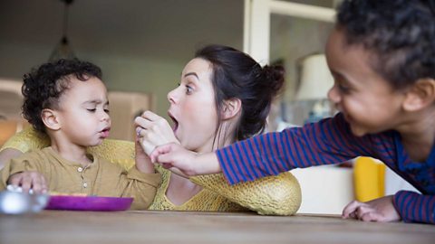 A playful mother feeding baby son at table.