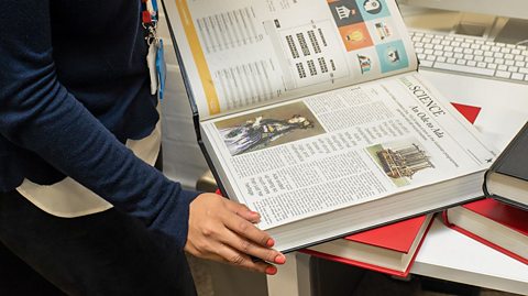 A science journal is held open, displaying articles on a table