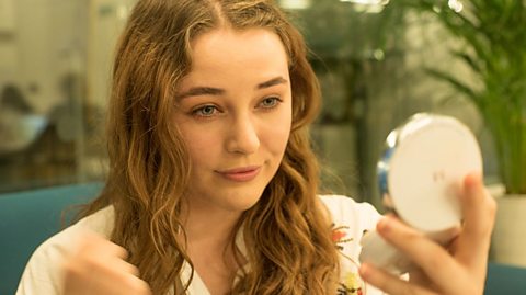 a young woman looks at herself in a hand held mirror