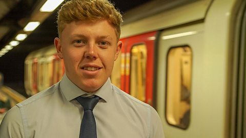 a young man stands on the platform next to a tube train in a London station