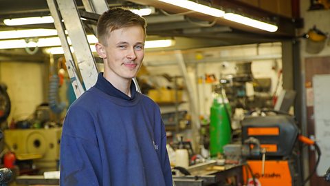 A young man stands in a metal workshop