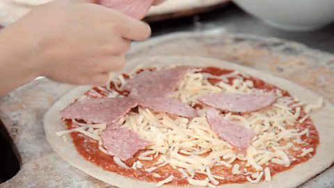 Someone putting toppings onto a pizza.