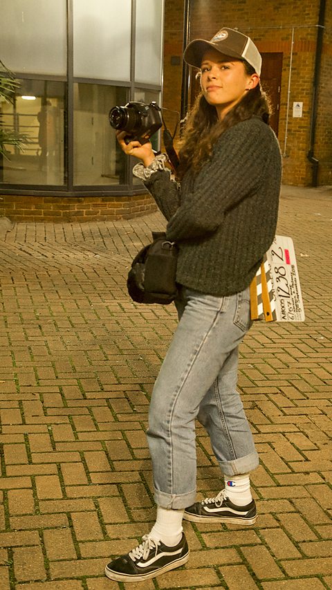 A young woman, Tamsin, standing outside with a camera and a clapper board