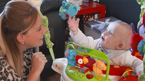 Mum Alison looking on as baby Austin gestures towards a toy