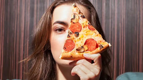 Getty A woman holds a slice of pizza (Credit: Getty)