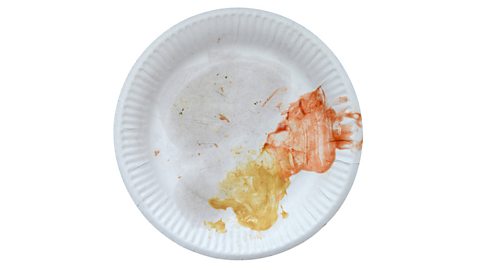 A disposable paper plate with food stains on it isolated on a white background.