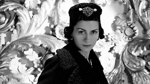 A black and white photograph of Coco Chanel wearing a coat and hat.