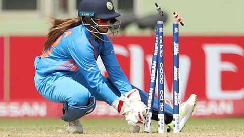 A female cricketer behind a wicket that's just been taken