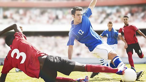 A football match in a stadium. Two footballers are kicking the ball.