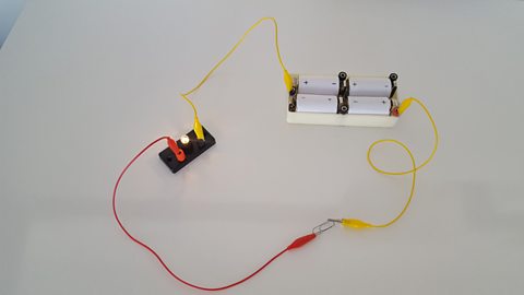 A simple circuit connects four batteries to a small lamp against a white background.
