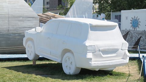 A life-size Styrofoam model of a car sits within a grassy area.