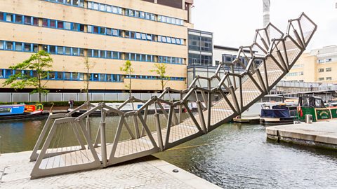 The Rolling Bridge, designed by Heatherwick Studios, is in place suspended over a river.