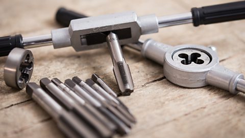 A metal tap and die set components, used to create threads, lie on a wooden table.