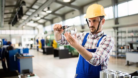 A worker in a hardhat uses a digital vernier caliper to conduct a quality control check.