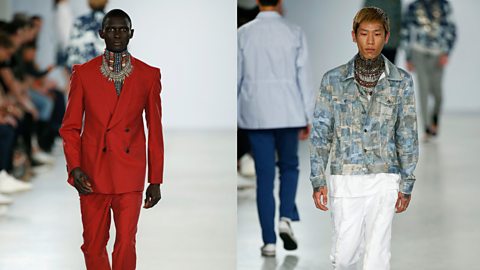 Two male models walk a runway, one in a bright red tailored suit and the other in a blue and white suit both designed by Joe Casely-Hayford.