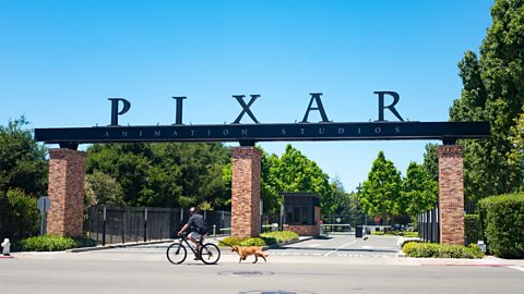 A man rides his bike and walks his dog past the Pixar Animation Studios headquarters.