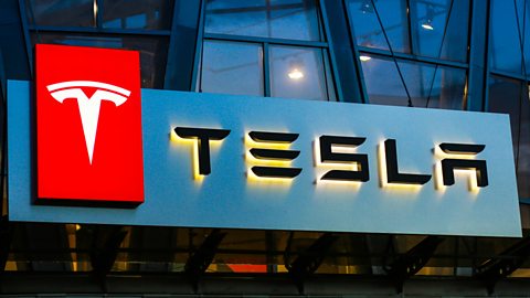 An illuminated Tesla storefront sign, showing the red and white logo and name in black.