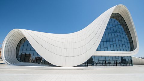 A white curved and glass-fronted building is a modern architectural design by Zaha Hadid.