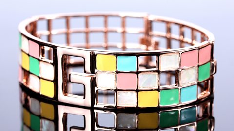 A brightly coloured enameled bracelet against a white background and reflected beneath it.