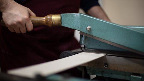 A man’s hands use an industrial guillotine to cut a long and thick piece of card.
