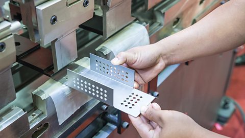 Hands hold a metal component to a machine that will hold and bend it.