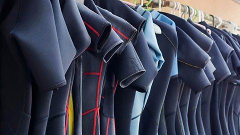 Many wetsuits are hung to dry on a clothing rail.