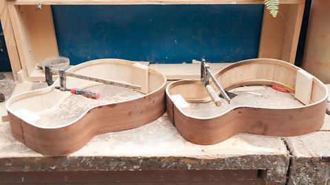 Two guitar bodies are in production, their formed curves being held in place by jigs.