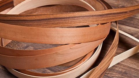 Different thin strips of veneer are in a rough pile against a wooden floor.