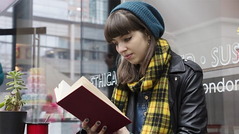 Young woman reads a book outside a cafe.