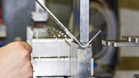 A worker operating a metal press machine to bend a piece of metal at a workshop.